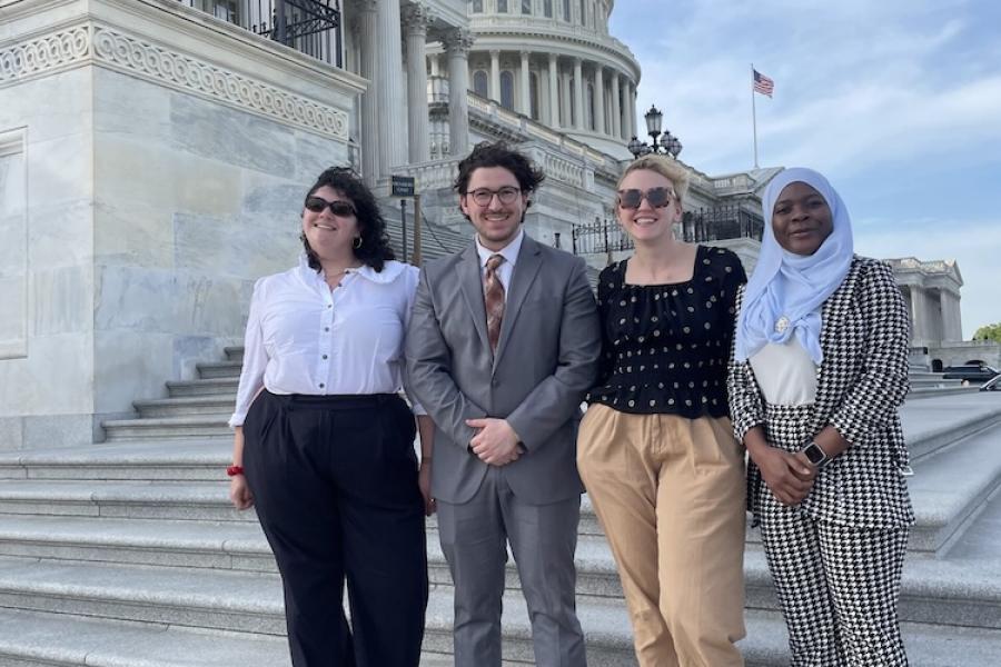 Four people stand on stone steps withe the dome of the U.S. Capitol building in the background