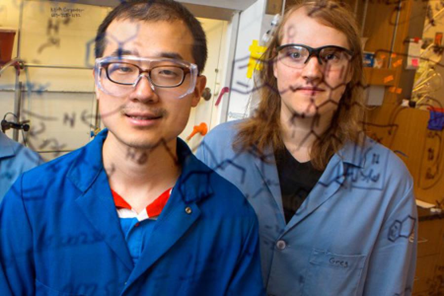 Two professors in lab coats looking at chemistry writing on a white board