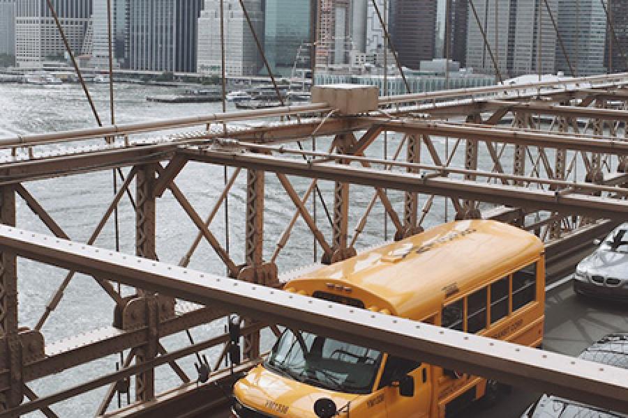 Yellow bus on a bridge, New York City in the background
