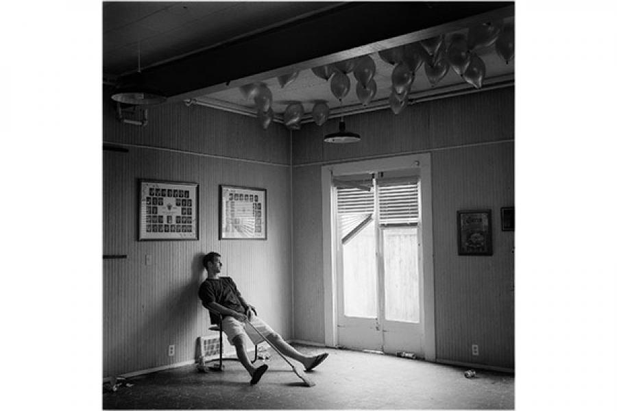 A fraternity brother sprawled in a chair in a nearly empty, half-wrecked room with balloons on the ceiling