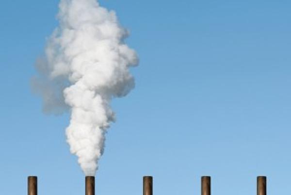 five smoke stacks against a blue sky; the second from left belches smoke