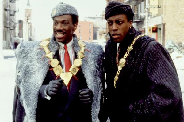 Two people -- characters in a film -- wearing large coats and gold jewelry