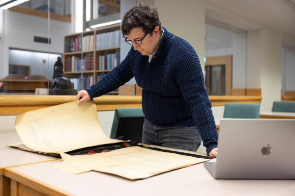 Person holds a large, yellowed document in a library setting