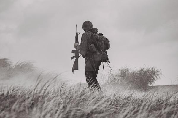 Soldier in uniform with backpack holding rifle walking across grasslands