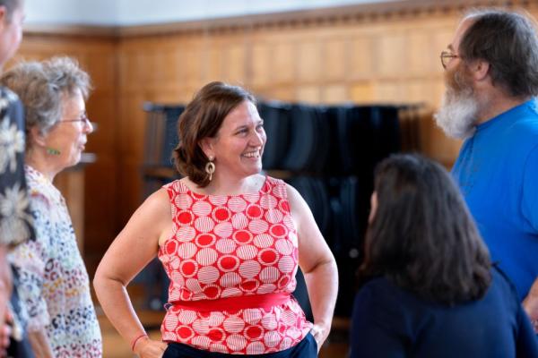 Person in red shirt smiles, hands on hips, while speaking with a circle of other people