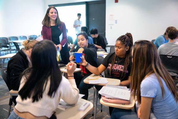 About six students sit in desks and interact using a blue Solo cup while an instructor stands by