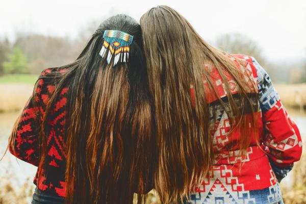 Two women with long hair and wearing Native American-patterned clothing and hairpiece.