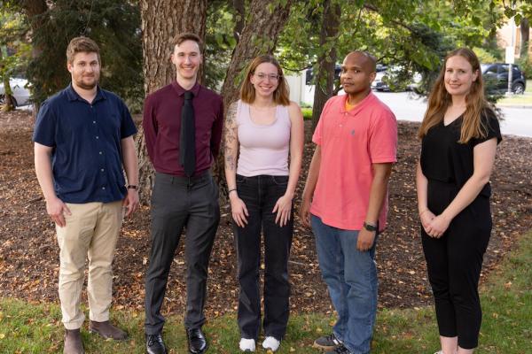 Five people standing in a line under a tree