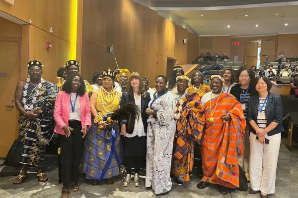 Sevral people, some in colorful traditional dress, stand together in an auditorium