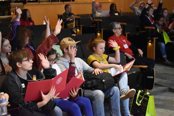 Bunch of students sitting in a room raising their hand 