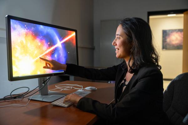 Anna Ho sitting at desk, pointing at computer screen with image of star exploding