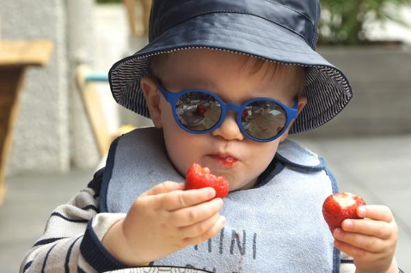 child wearing sunglasses, holding two strawberriers