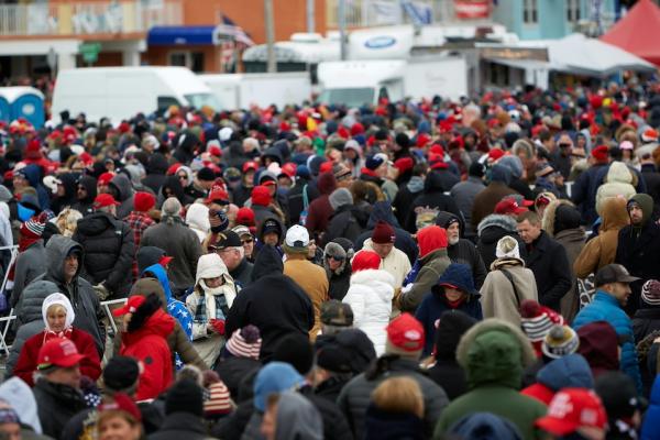 hundreds of people crowded together, waiting for a public event to being. It is cold; most of them wear hats and coats