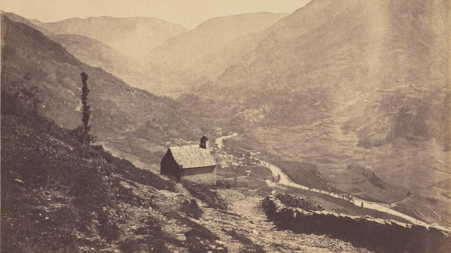 sepia-toned photograph showing mountains and a small house