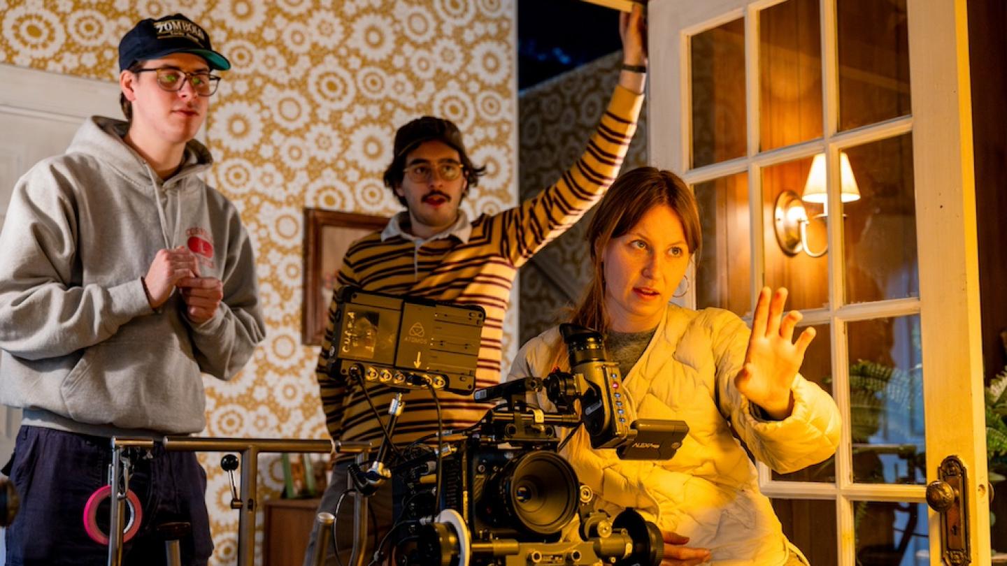 Three people who are making a movie look over the top of a large film camera