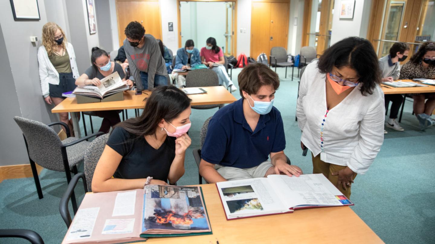 Three people leaning over open books on a table, in a library
