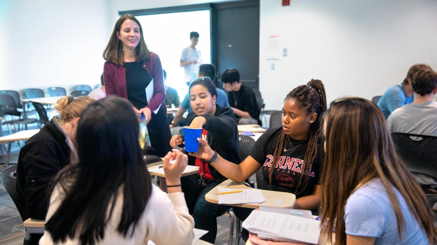 About six students sit in desks and interact using a blue Solo cup while an instructor stands by