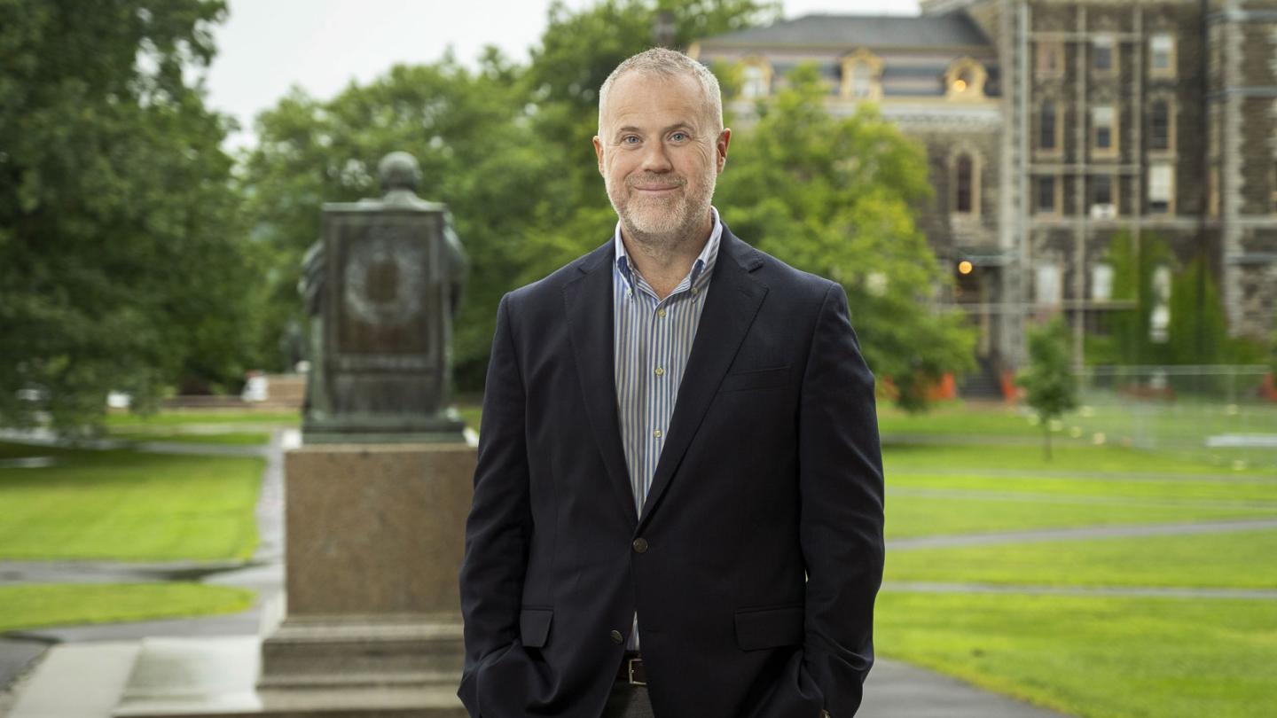 Dean Peter Loewen posing behind the A.D. White statue on the Arts Quad