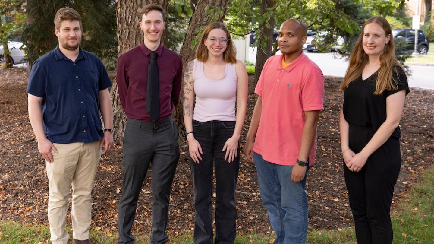 Five people standing in a line under a tree