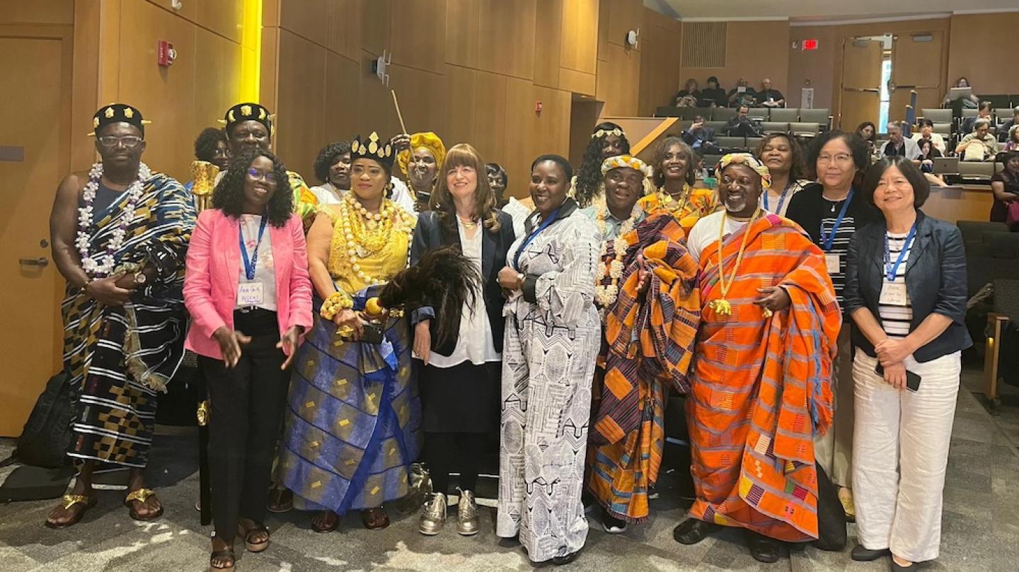 Sevral people, some in colorful traditional dress, stand together in an auditorium