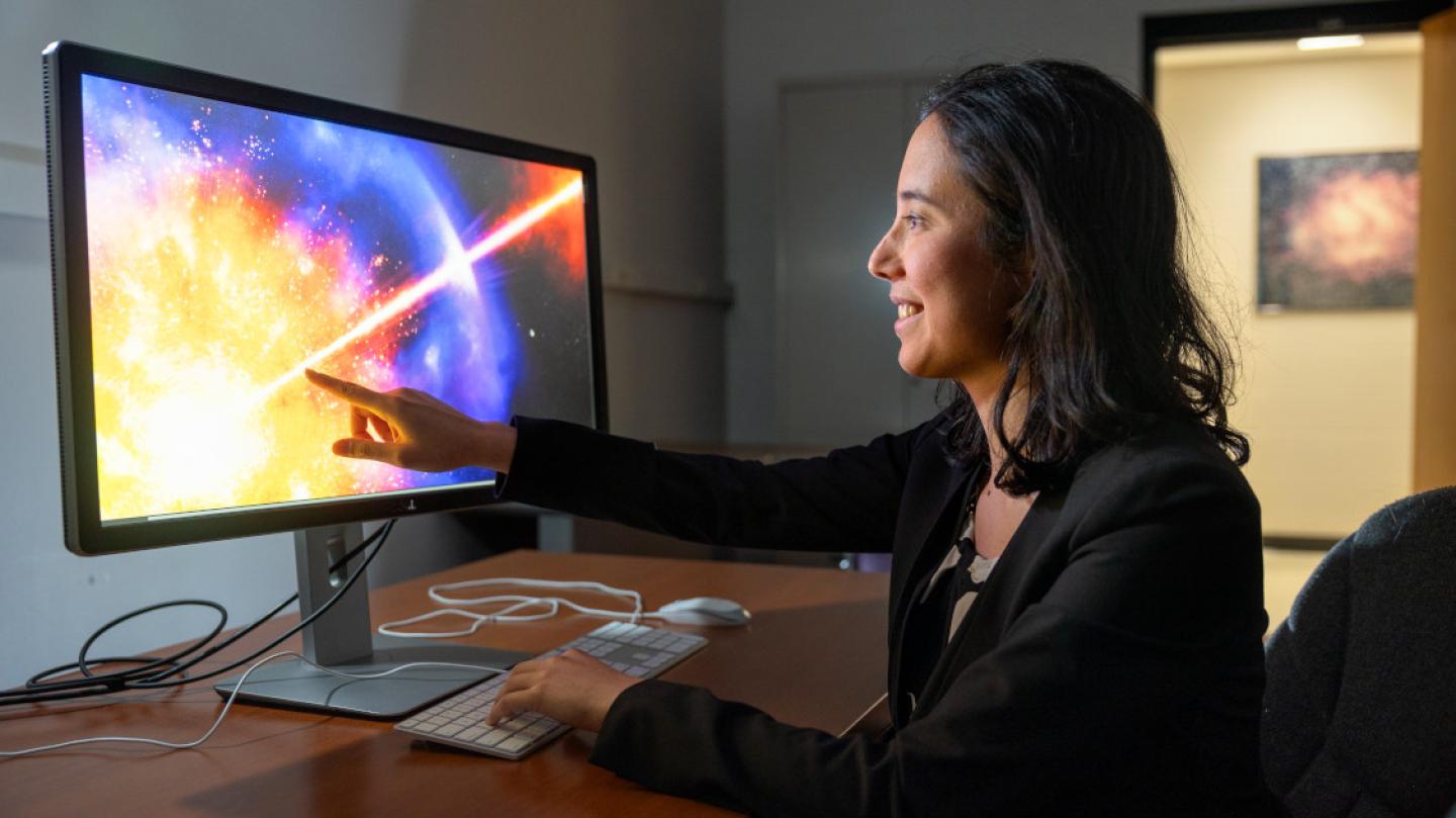 Anna Ho sitting at desk, pointing at computer screen with image of star exploding
