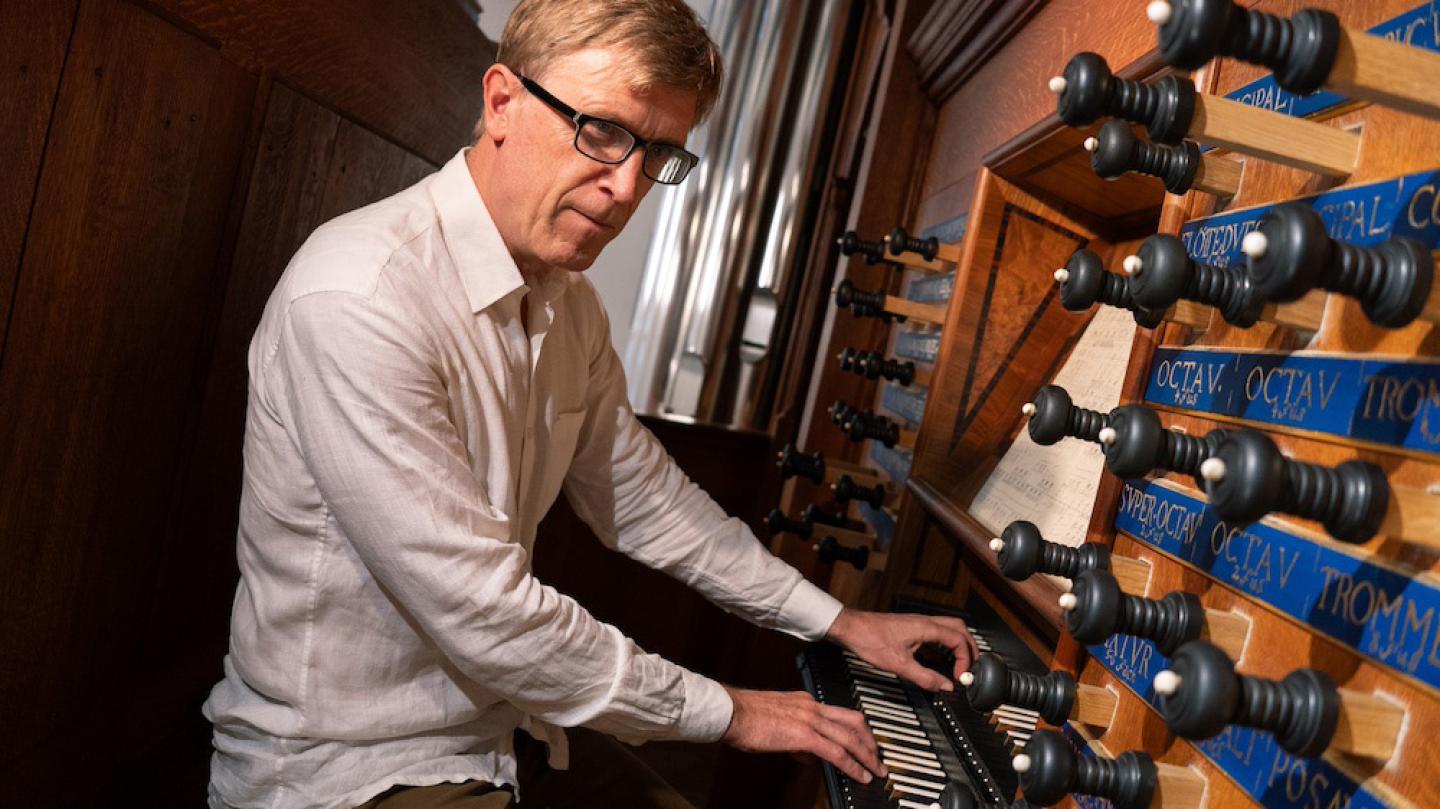 Person sitting at the consol of a wooden organ, hands on keyboard