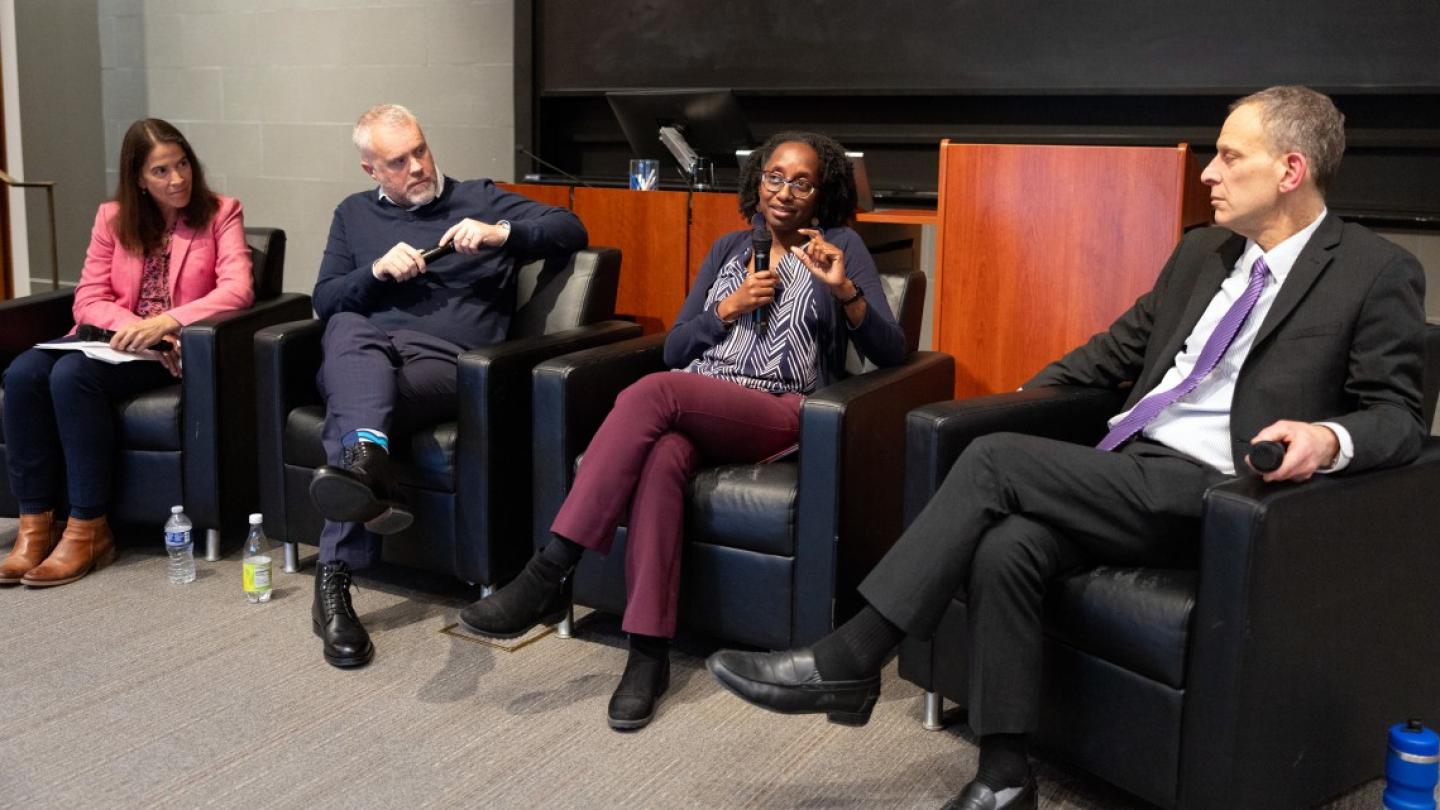 The panelists sitting in arm chairs, all three looking at Prof. Jamila Michener talking into the microphone.