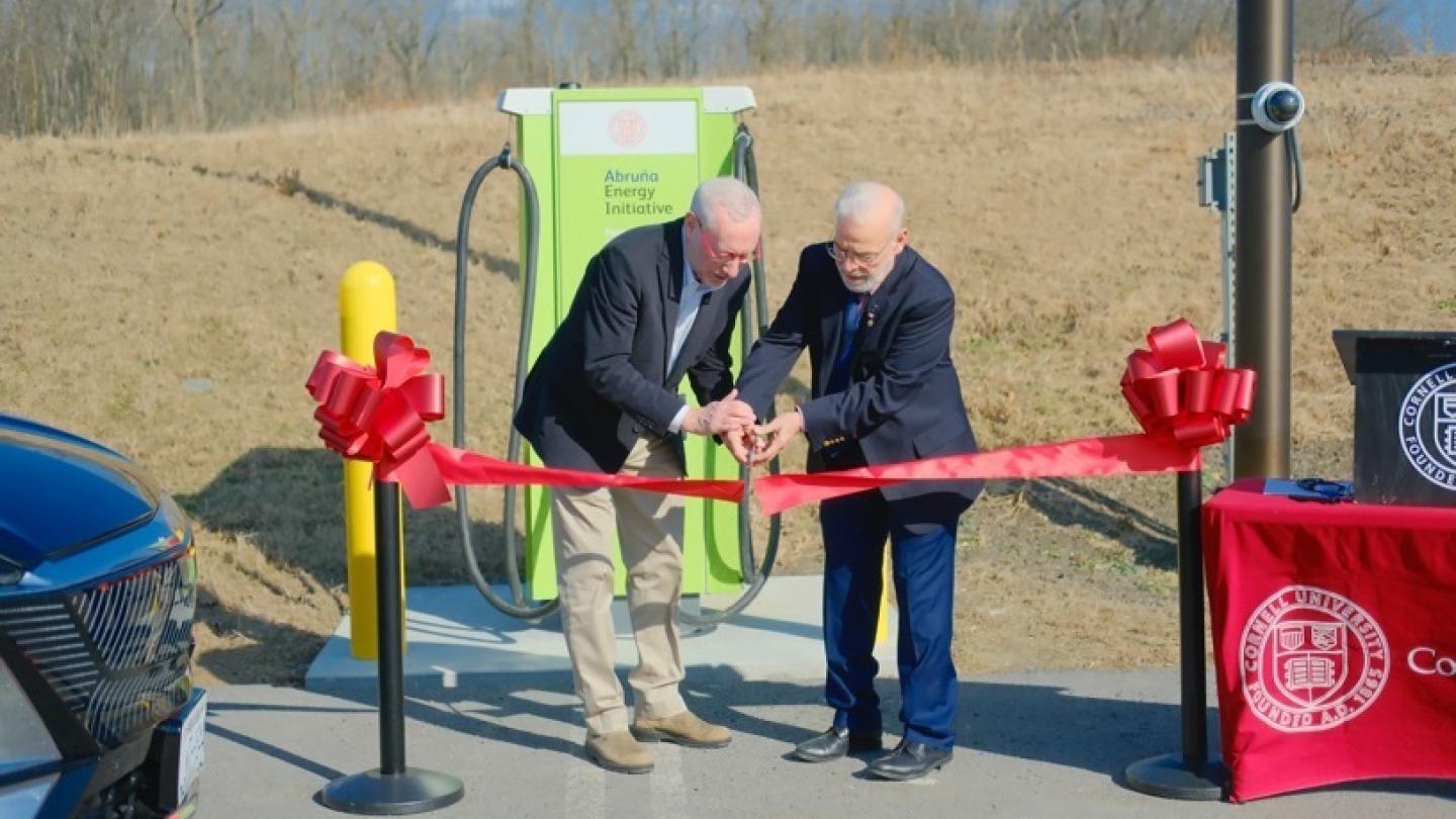 Two people cutting a red ribbon ceremonially. They are outdoors