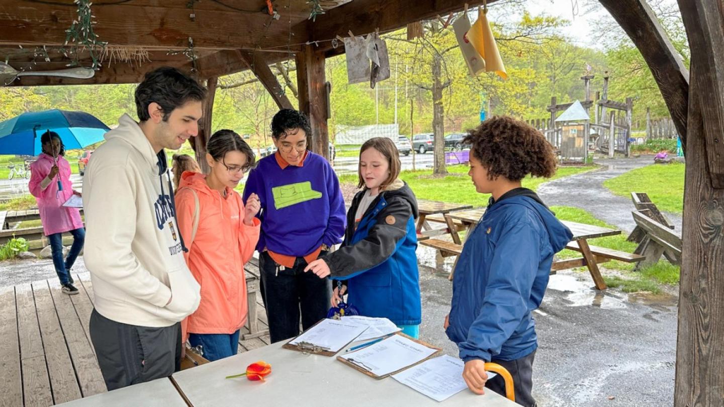 People cluster together in an outdoor shelter, looking at papers and flowers