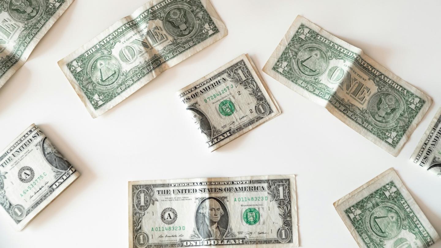 Dollar bills, some of them folded and crumpled, resting on a white surface