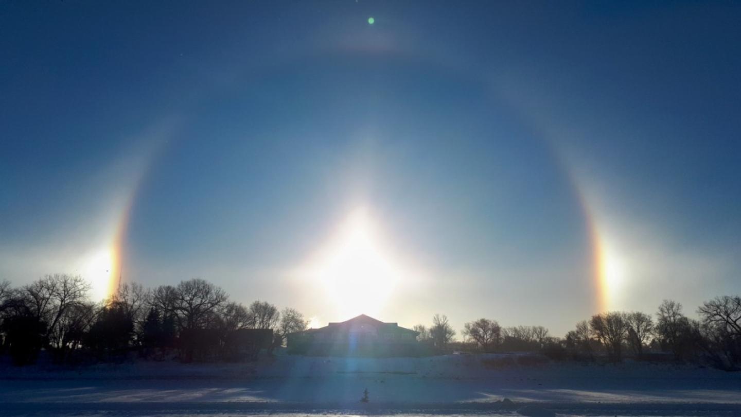 In the sky, a perfect half circle appears around a rising sun with two bright "sun dogs" on either side