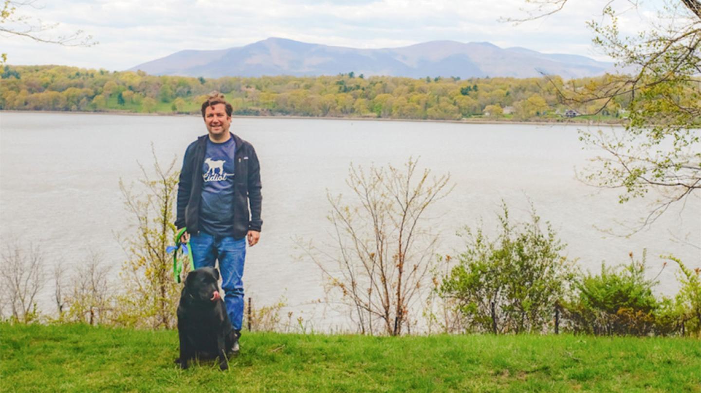 Person standing with a dog on the bank of a river