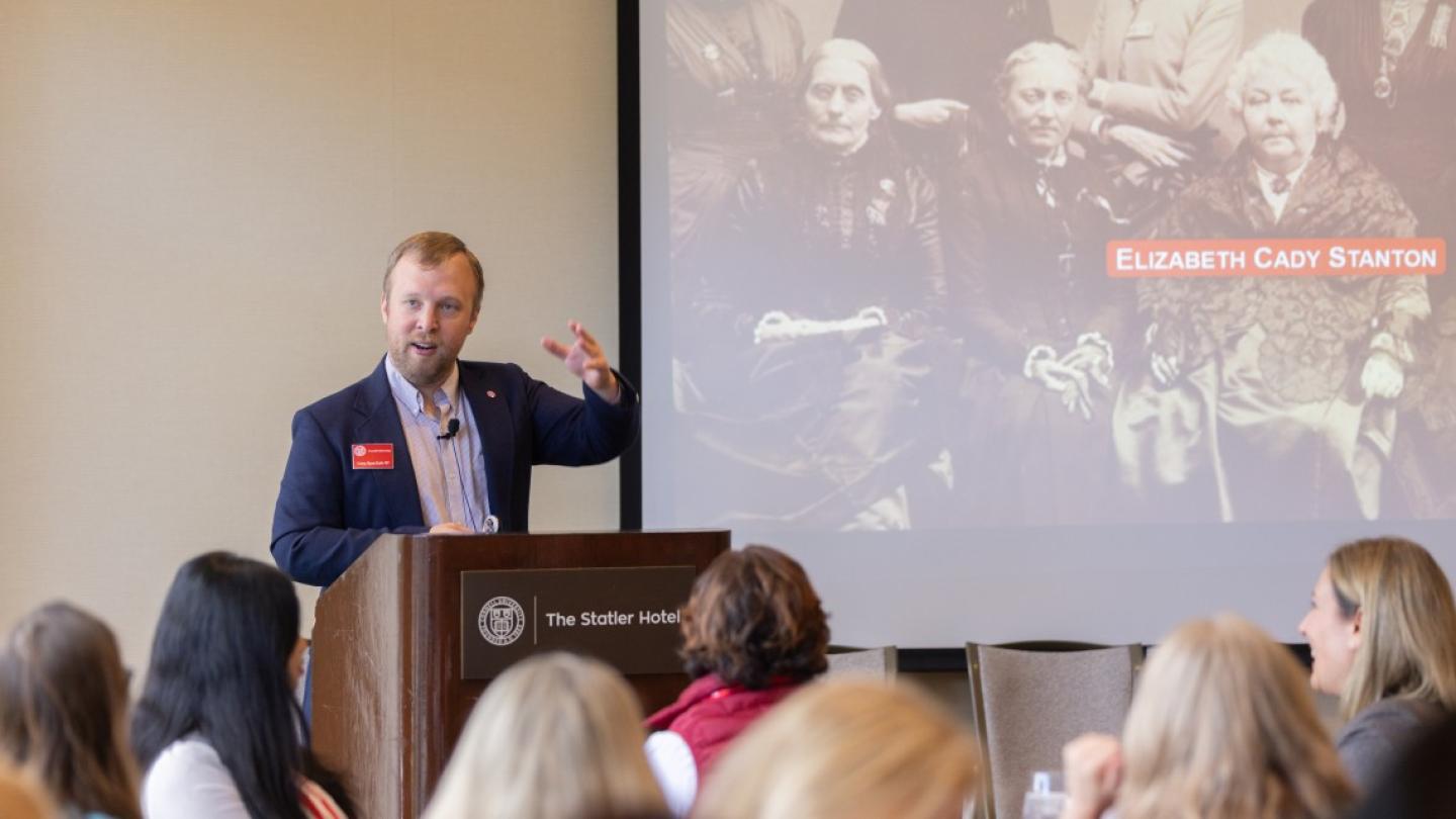 Person speaking at a lecturn with a black and white photograph displayed behind