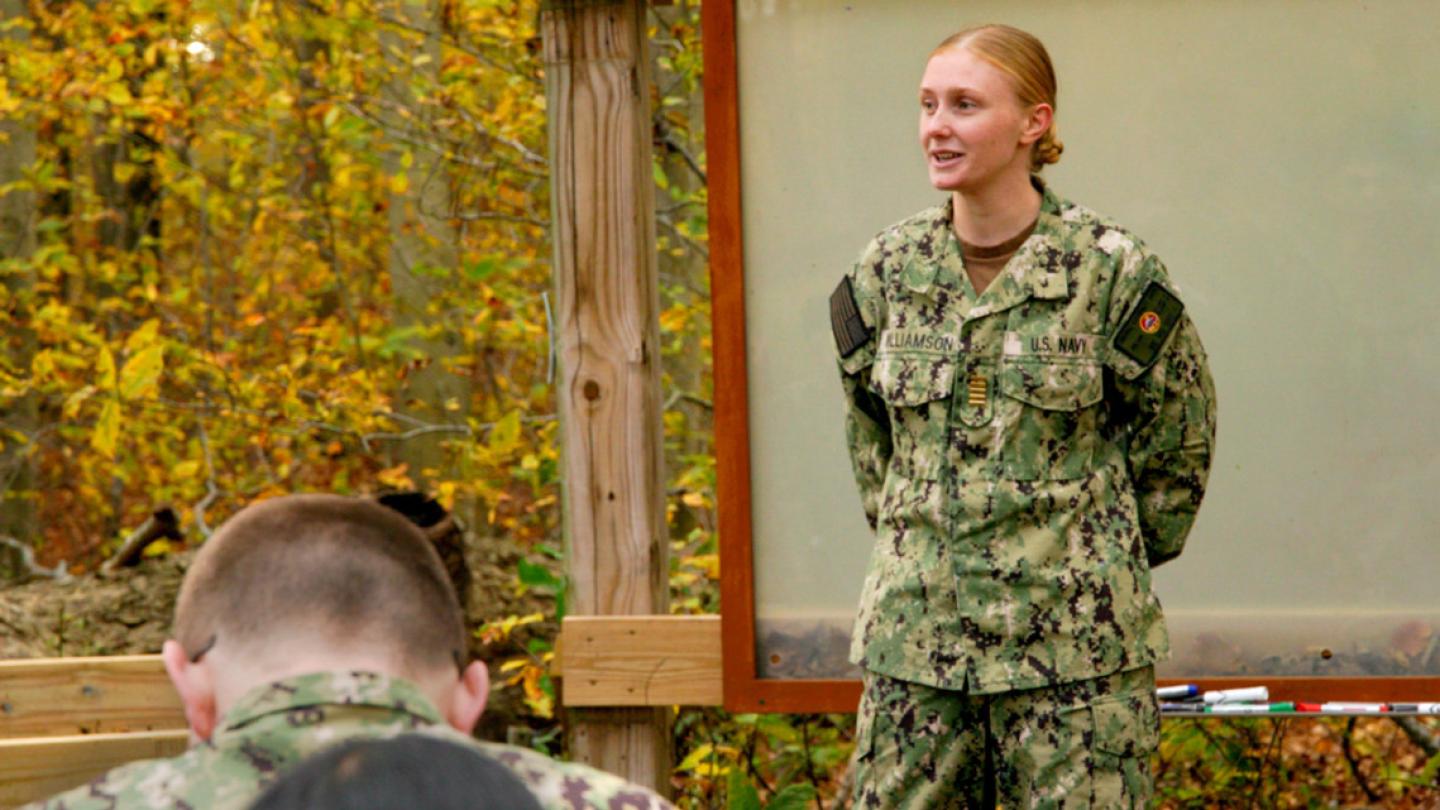 Person in military fatigues standing in front of others, speaking