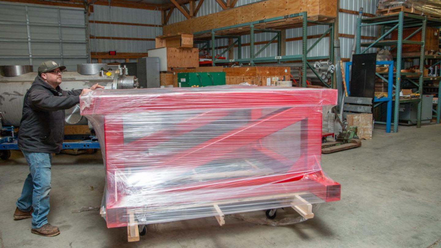 Person pushing, on a dolly, a large red frame wrapped in plastic